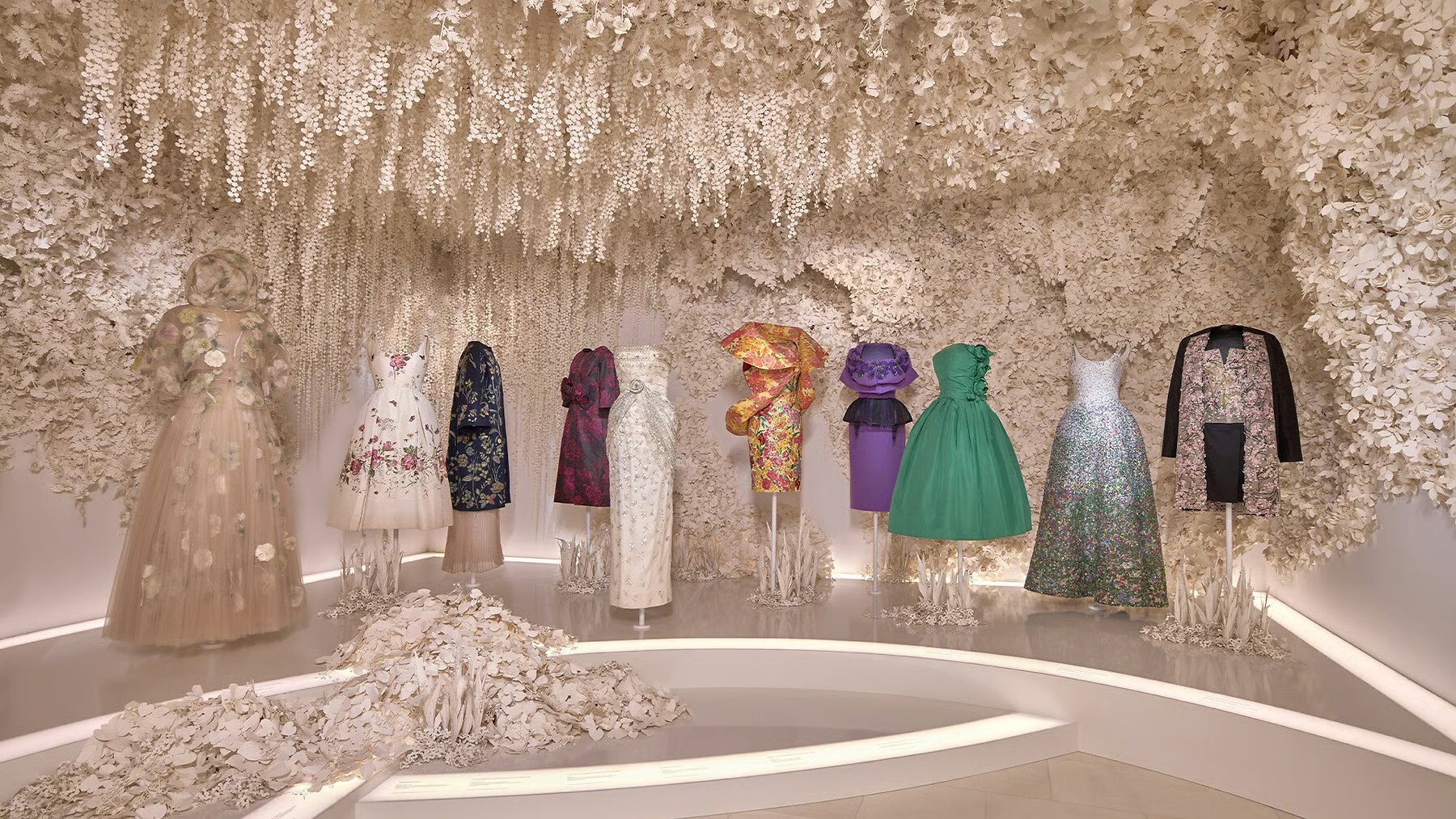 Roupas elegantes expostas em ambiente decorado com flores brancas, lembrando Christian Dior Jardins Rêves.