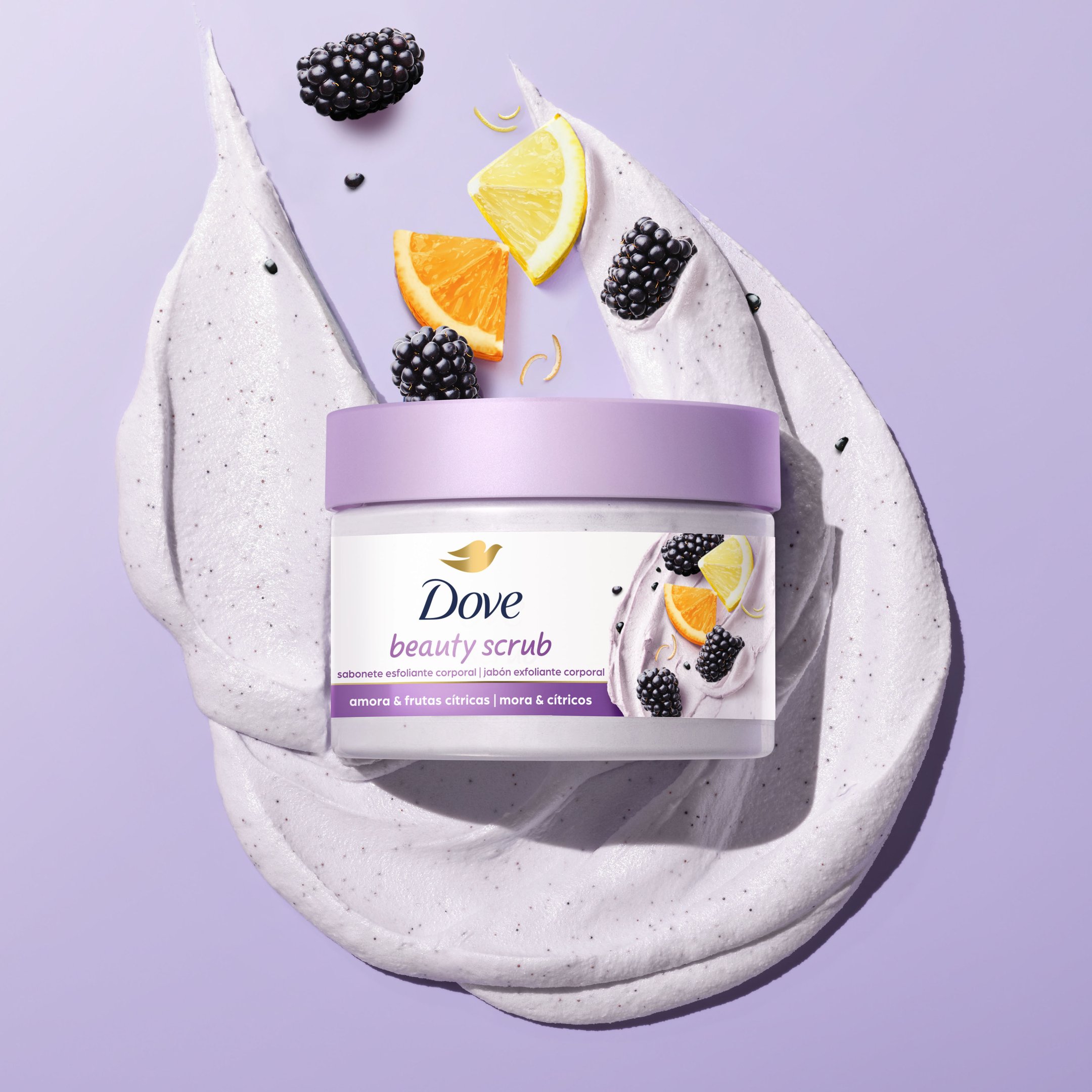 Esfoliante corporal Dove com amoras e fatias de laranja sobre creme lilás espalhado.
