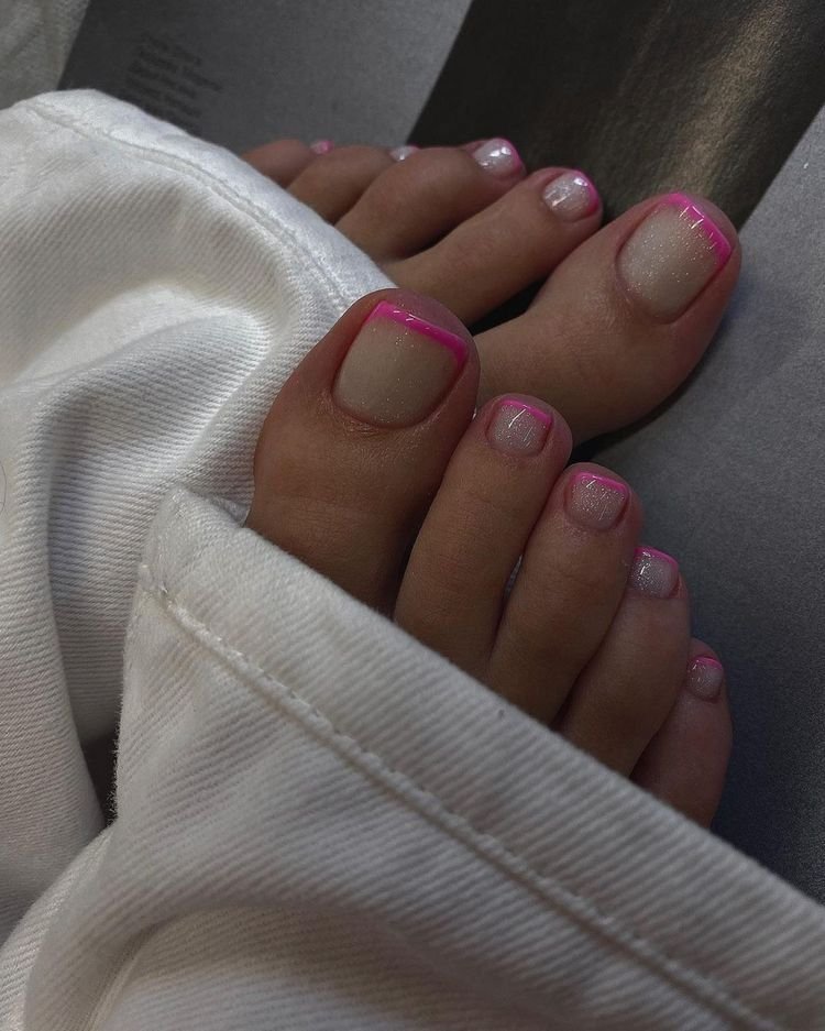 Unhas dos pés com esmalte estilo francesinha no pé, bordas rosa, em destaque sobre tecido branco.