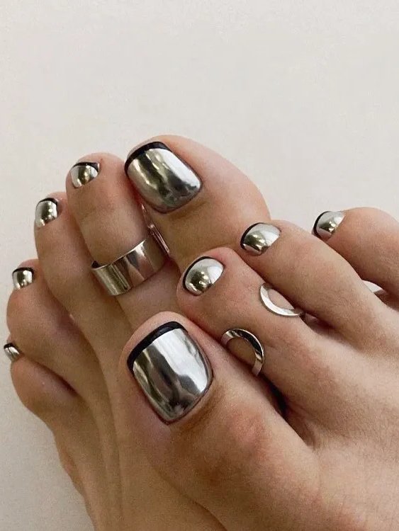 Unhas desenhadas com esmalte cromado e francesinha no pé preta. Anéis decorativos nos dedos dos pés.
