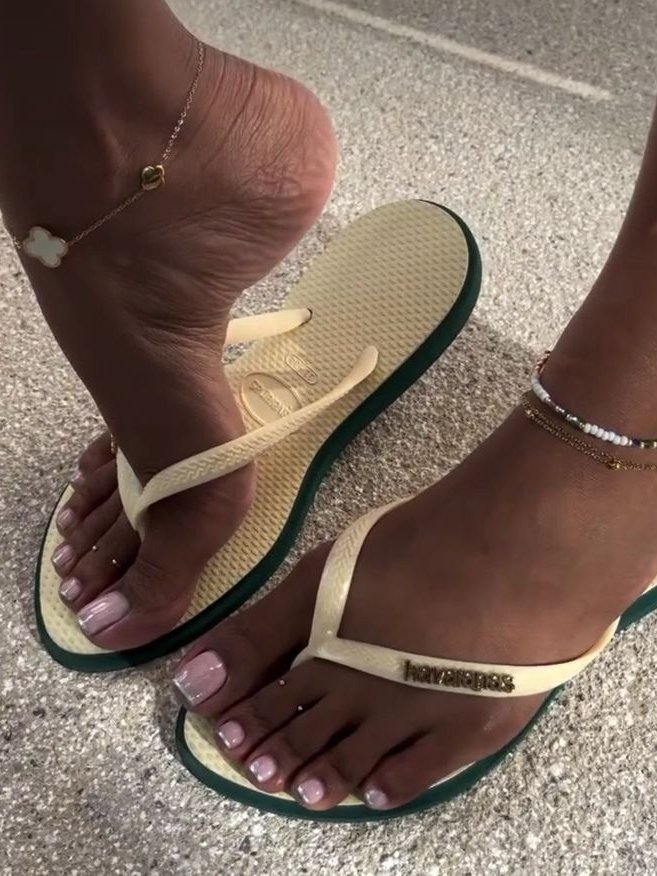 Unhas dos pés com esmalte estilo francesinha no pé, usando sandálias claras com tornozeleiras.