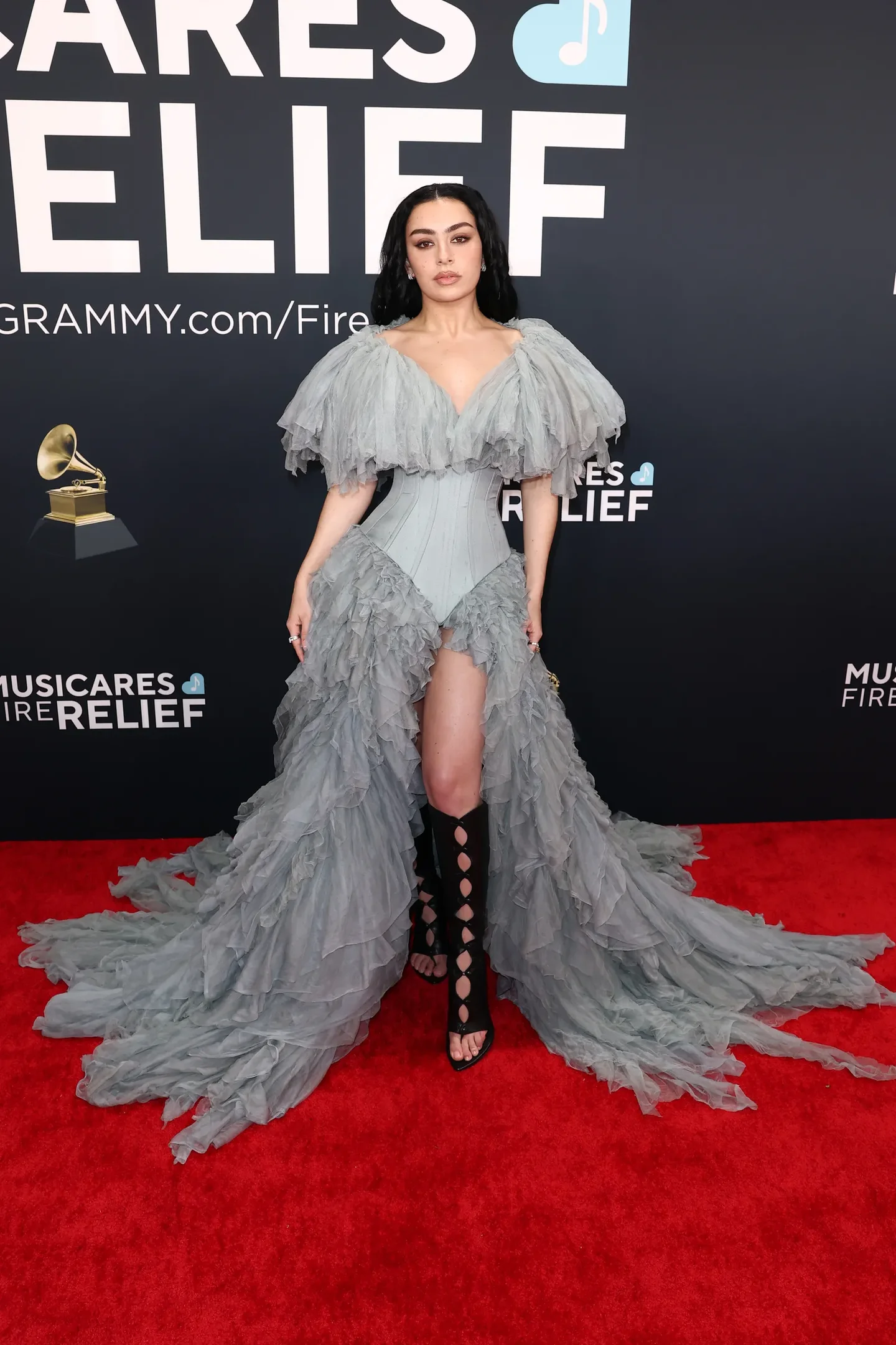 Pessoa usando vestido volumoso cinza e sandálias estilo gladiadora pretas em tapete vermelho de evento de música.