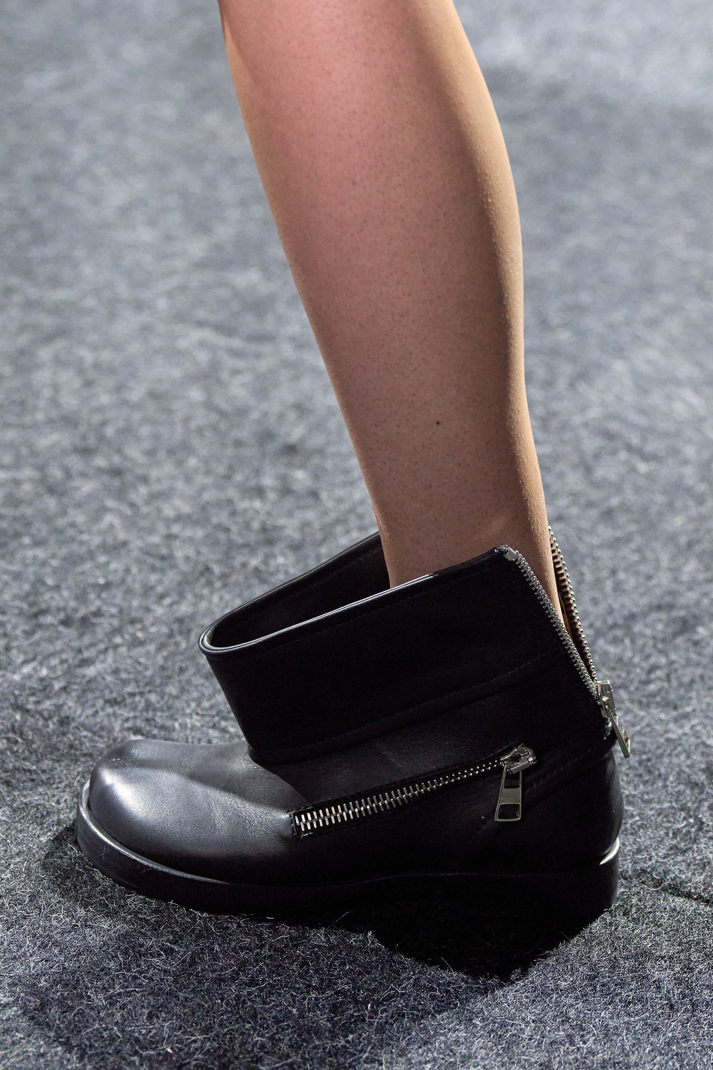 Bota preta com zíper e cano franzido, destacando-se sobre tapete cinza.