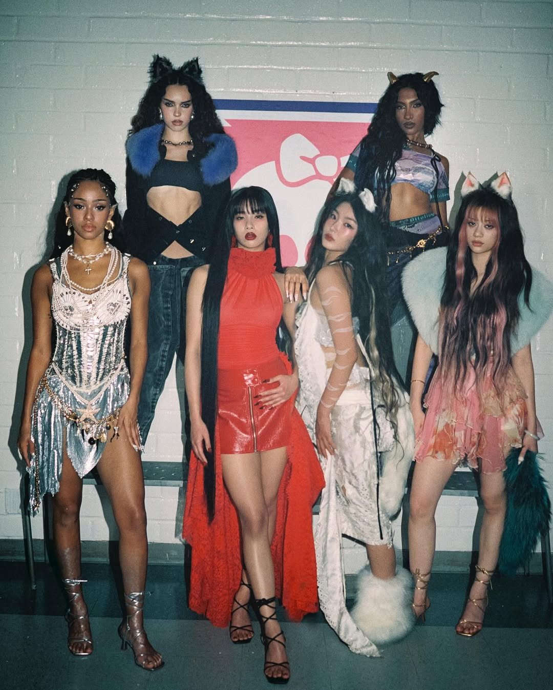 Seis pessoas posam em roupas glamorosas com acessórios de orelhas de gato, refletindo estilo katseye.