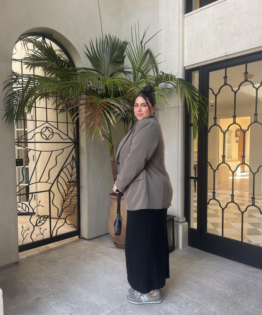 Pessoa com estilo Lazy dressing, usando blazer, saia longa preta e tênis, em um ambiente interno com plantas.