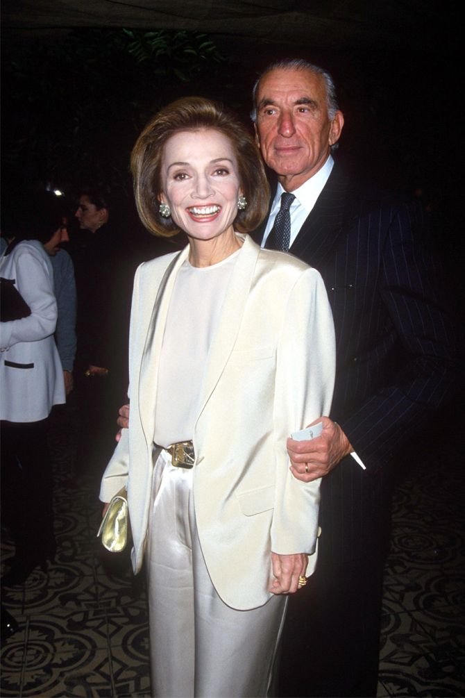 Lee Radziwill sorrindo em um evento formal, ambos em trajes elegantes.
