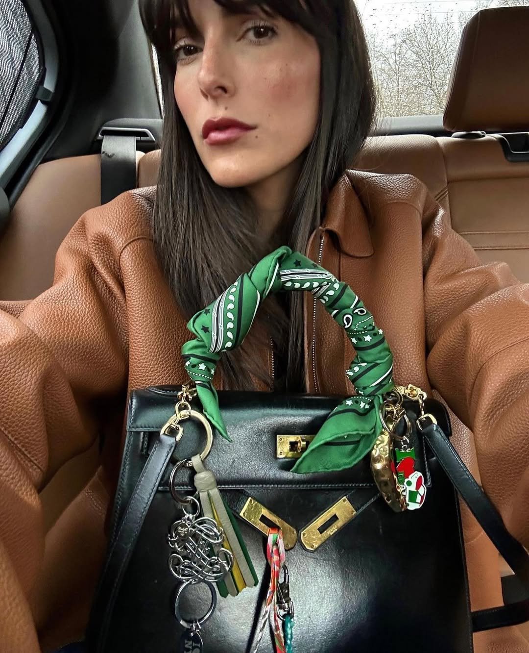 Mulher em um carro segura bolsa com alça decorada com lenço verde estampado.