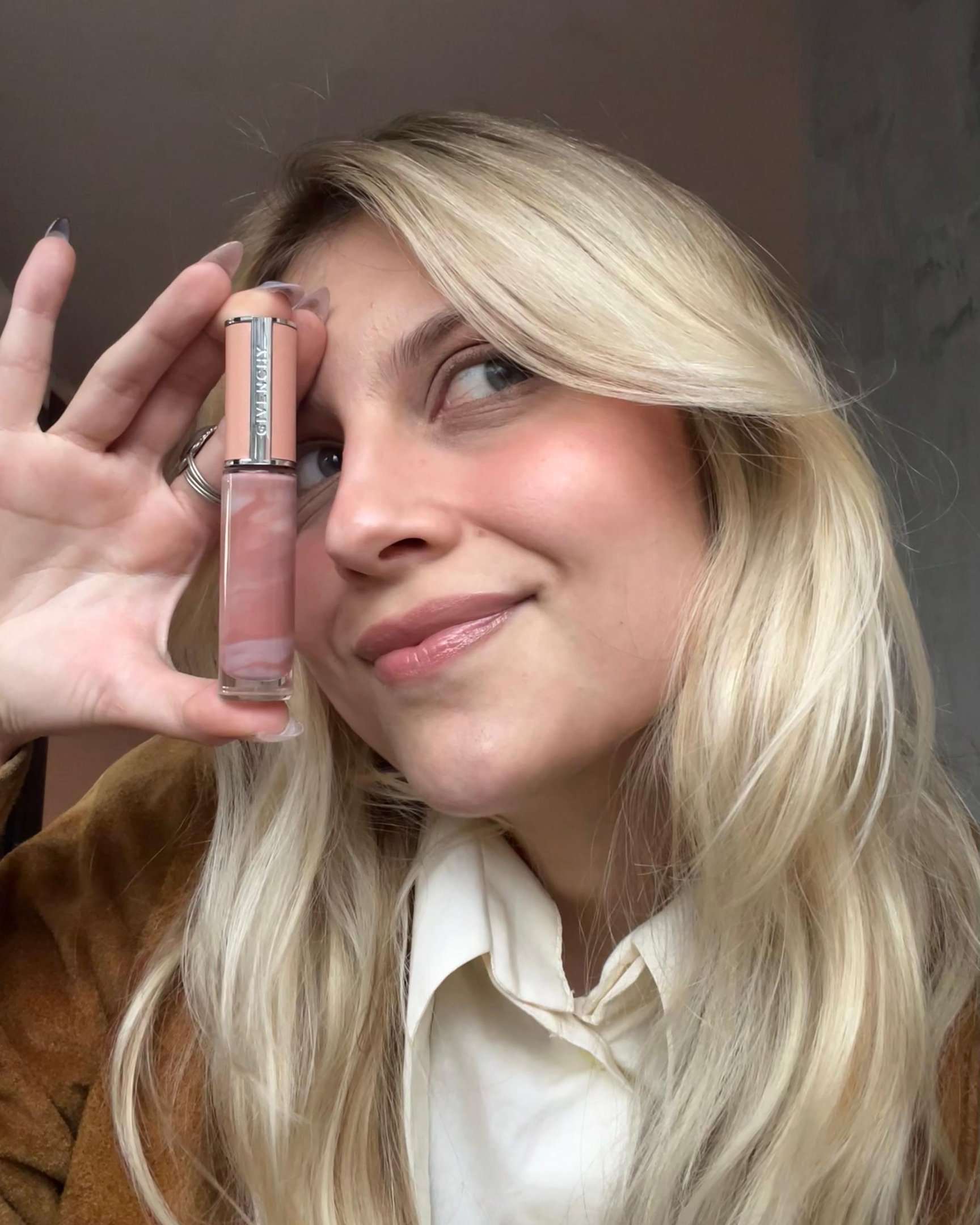 Usuária loira sorrindo segura um lip balm rosa ao lado do rosto.