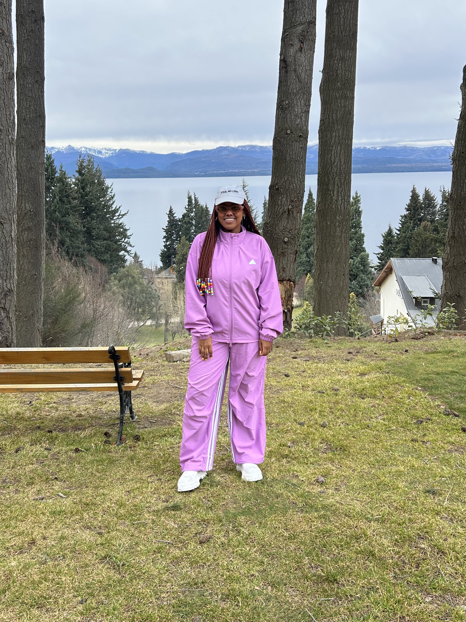 Pessoa usando conjunto esportivo lilás em cenário natural com árvores e lago ao fundo. Looks de inverno coloridos