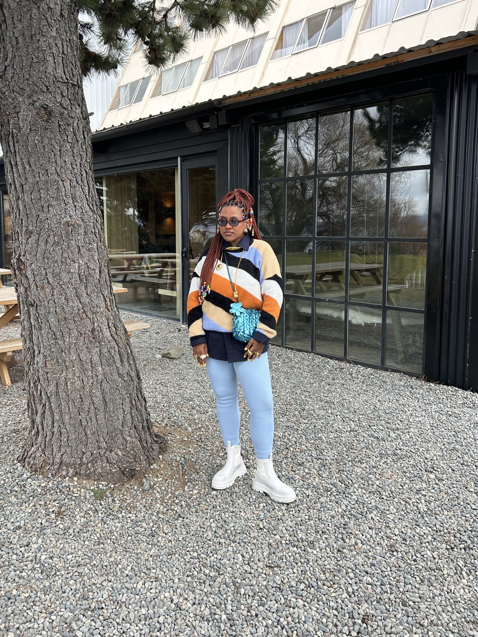 Pessoa com suéter listrado colorido, calça azul clara e botas brancas em ambiente externo. Looks de inverno coloridos.