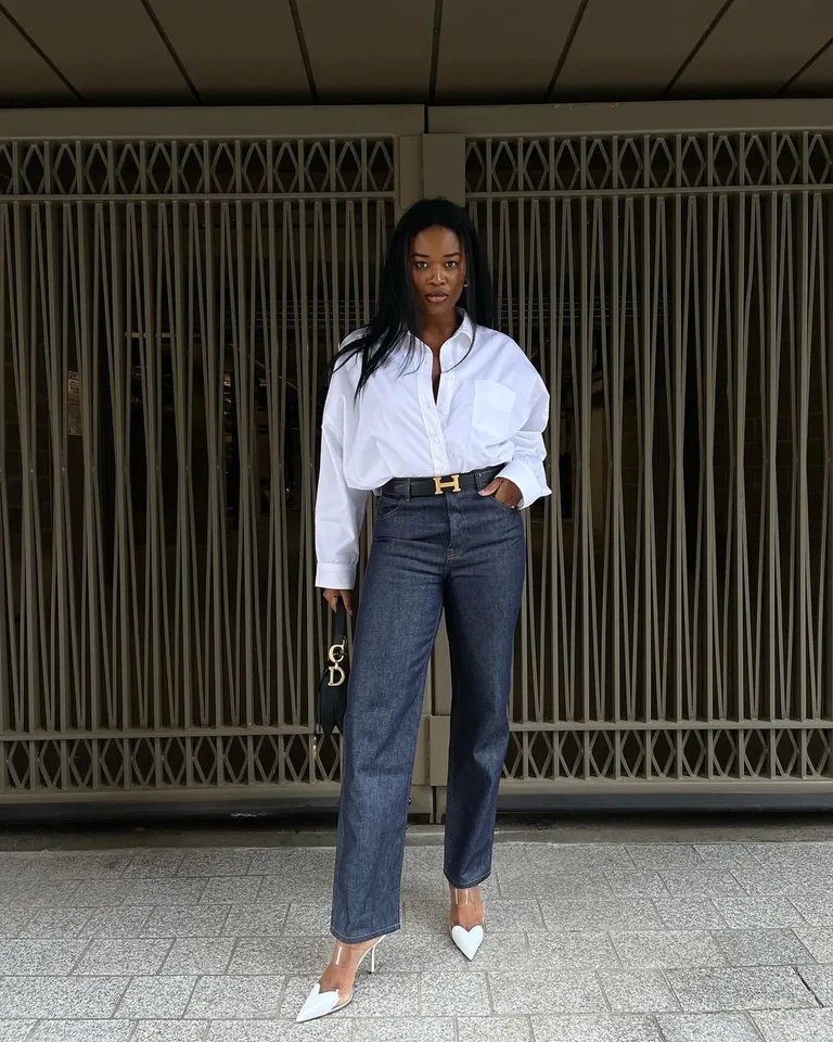 Mulher com look noturno de calça jeans, camisa branca, sapatos brancos e cinto preto.