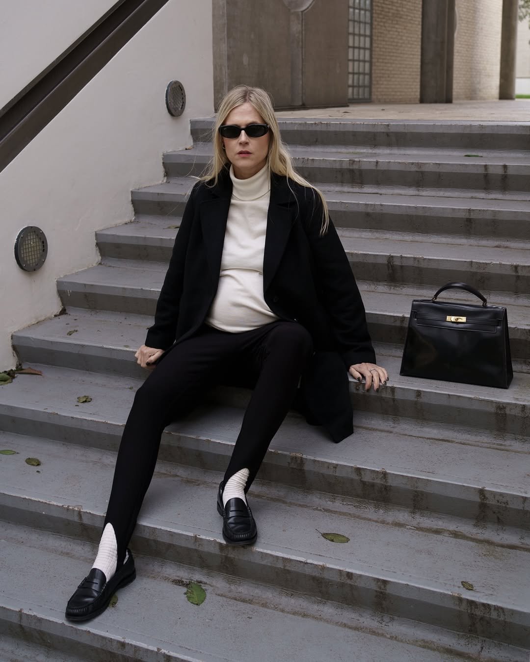 Pessoa sentada em escada, usando óculos escuros e legging fusô, acompanhada de bolsa preta. Representando looks com calça legging fusô.