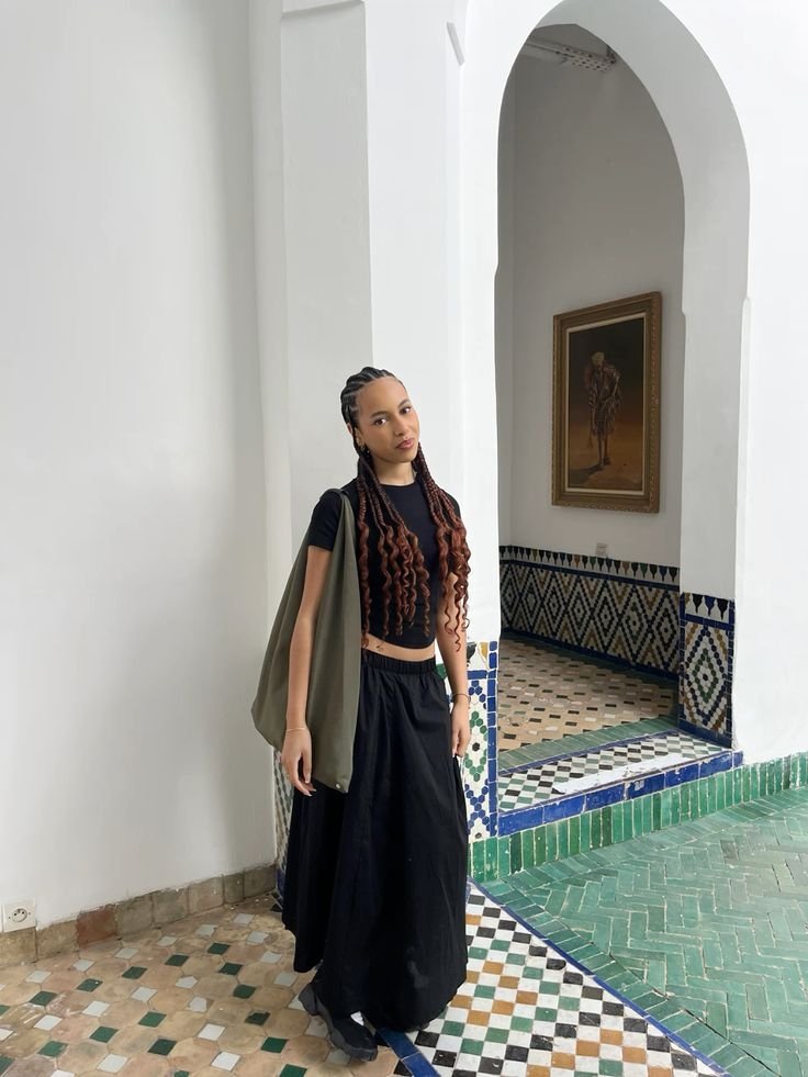 Pessoa de tranças longas, em roupa preta, posando em espaço com azulejos decorativos. Associações com Nike Air Rift não são visíveis.