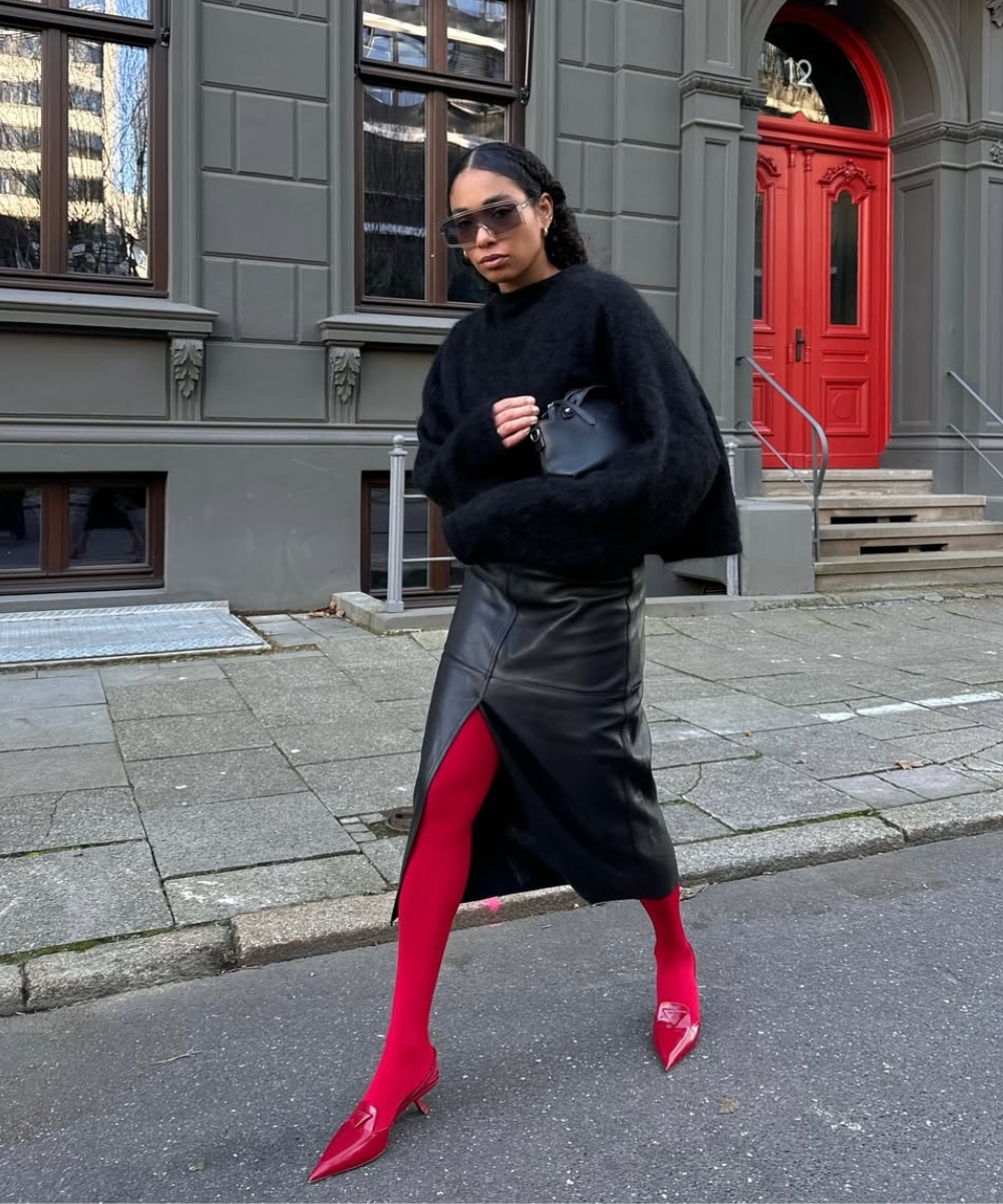 Pessoa usando saia preta de couro, suéter preto e meia-calça vermelha. Look de inverno sofisticado.