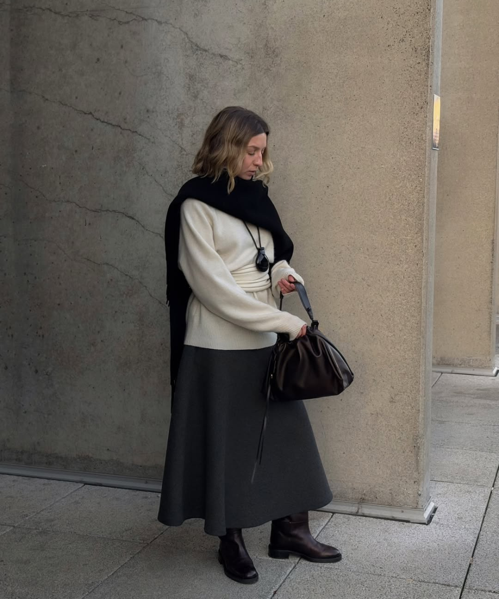 Mulher com suéter e saia escura, lenço preto e botas, exemplificando looks de inverno com saia.
