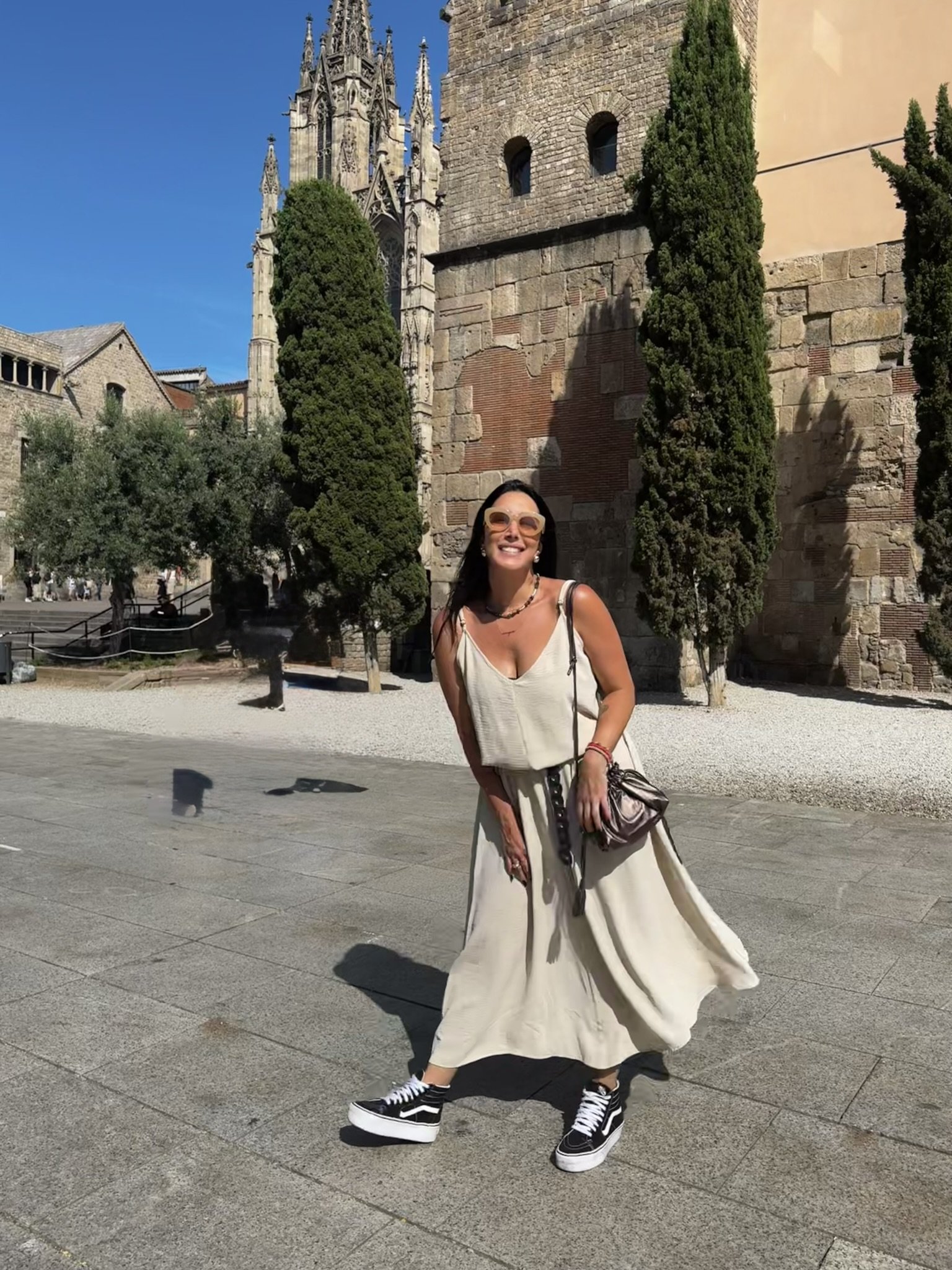 Mulher sorrindo em vestido leve em frente a catedral histórica, céu azul e clima de verão europeu.