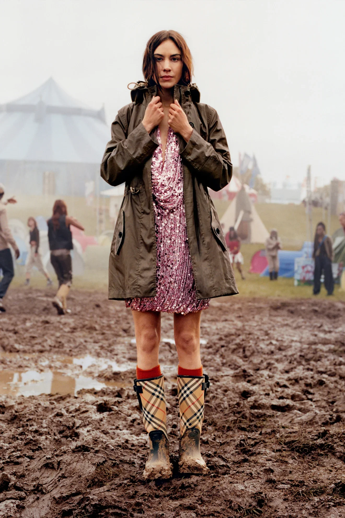 Pessoa de casaco e vestido brilhante, em festival com lama. Ela usa botas estampadas. Chinelo de dedo