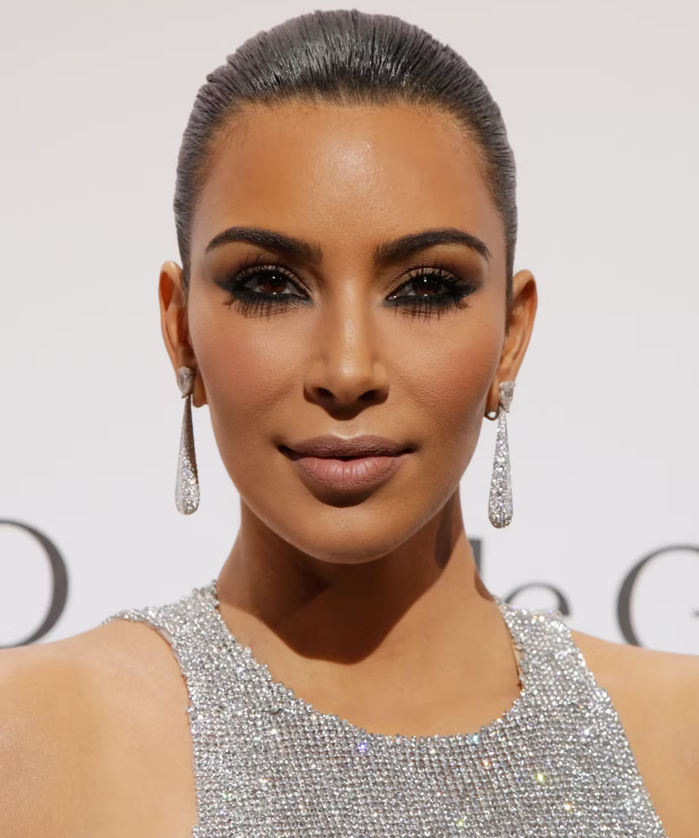 Mulher com maquiagem sofisticada e penteado elegante, usando técnica de contorno, veste vestido brilhante e brincos longos.