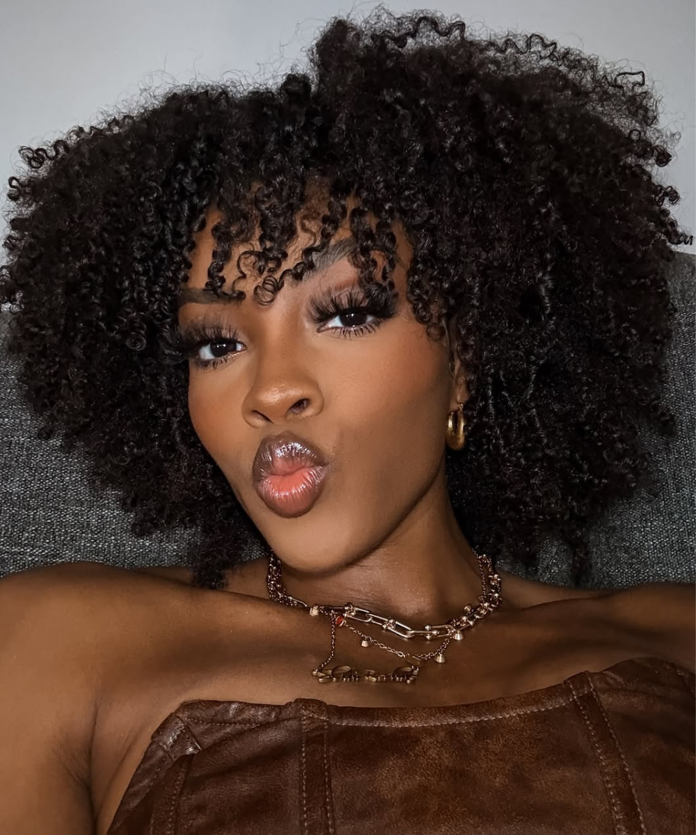 Mulher com cabelo crespo volumoso e maquiagem destacada. O cabelo bem cuidado sugere que ela usa o melhor óleo para cabelo crespo.