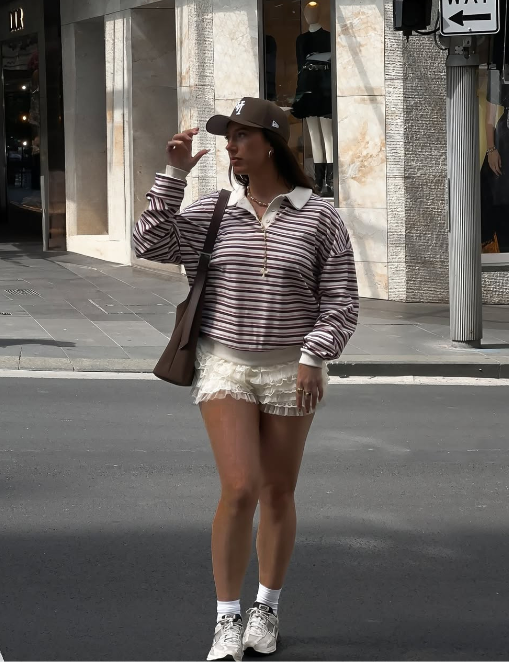 Mulher usando boné e suéter listrado caminha pela cidade em dia típico de Verão 2026.
