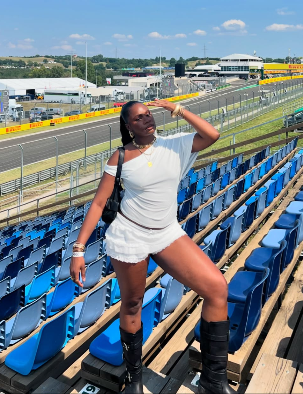 Pessoa em arquibancada de corrida sob sol forte usando roupas claras e botas. Verão 2026.