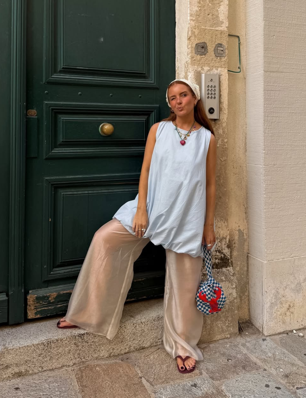 Jovem com look casual de calça larga e blusa azul. Sentada diante de uma porta. Moda inspirada no Verão 2026.