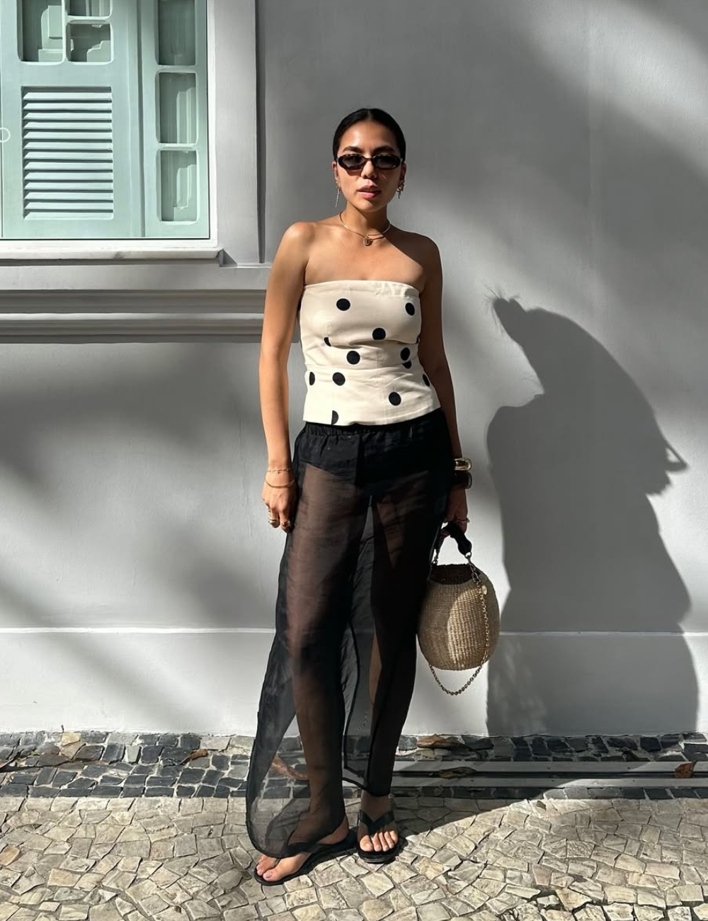 Pessoa usando top de bolinhas e saia transparente, segurando bolsa de palha. Moda inspirada no verão 2026.