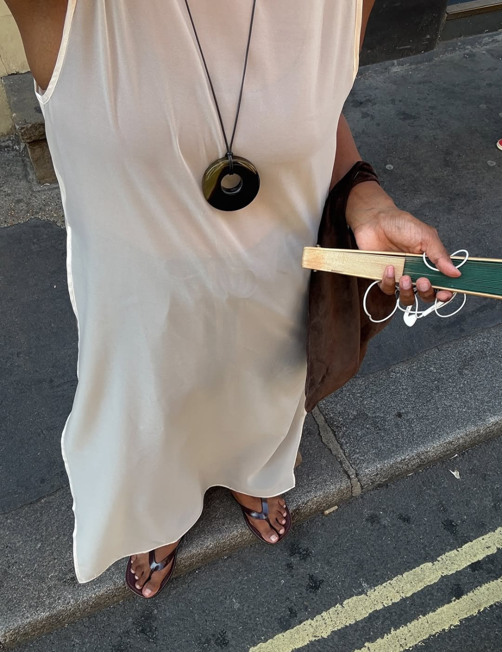 Vestido branco leve, colar circular preto, sandálias marrons. Pessoa segura leque. Estilo casual para Verão 2026.