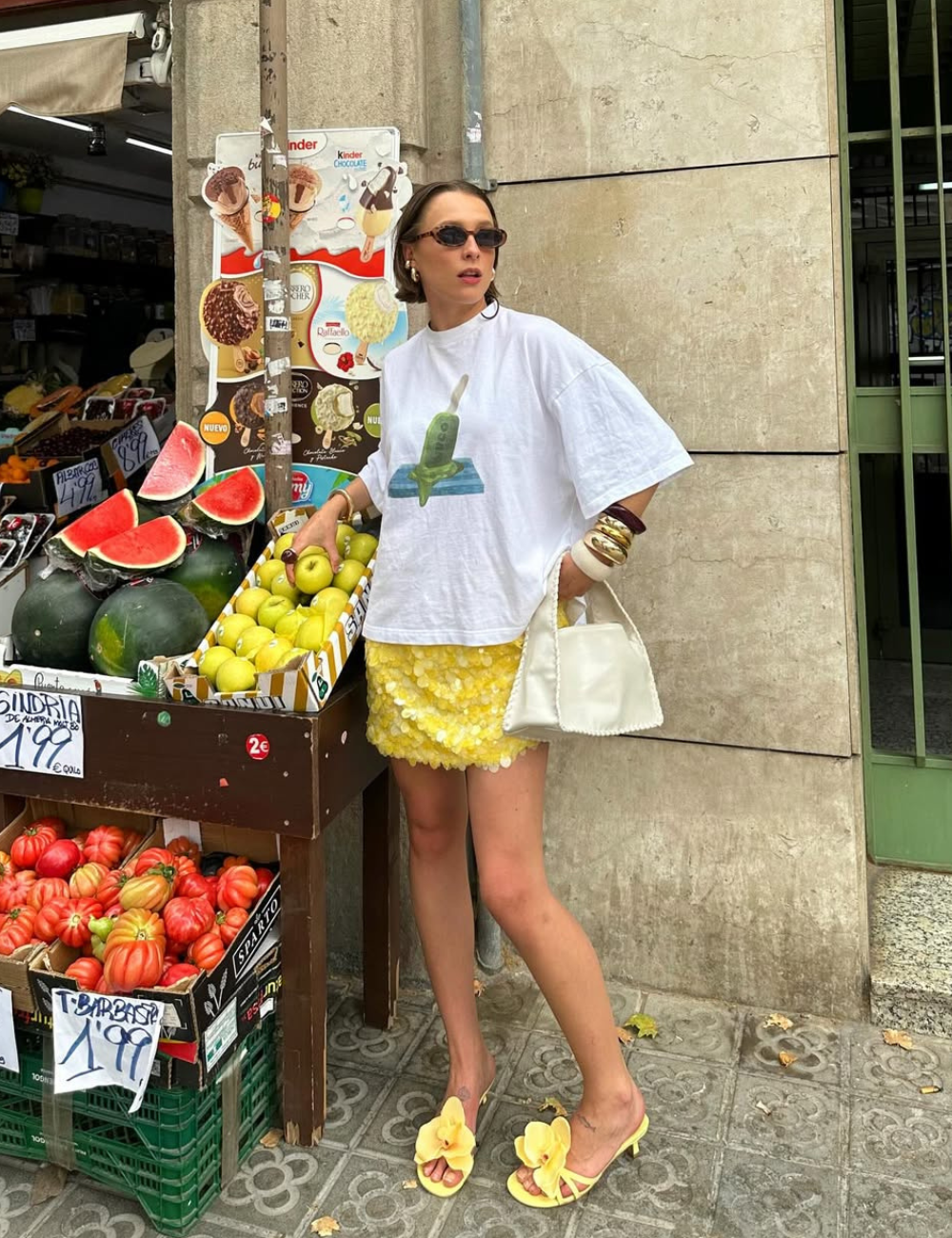 Pessoa em frente a barraca de frutas usando camiseta e saia amarela, moda Verão 2026.