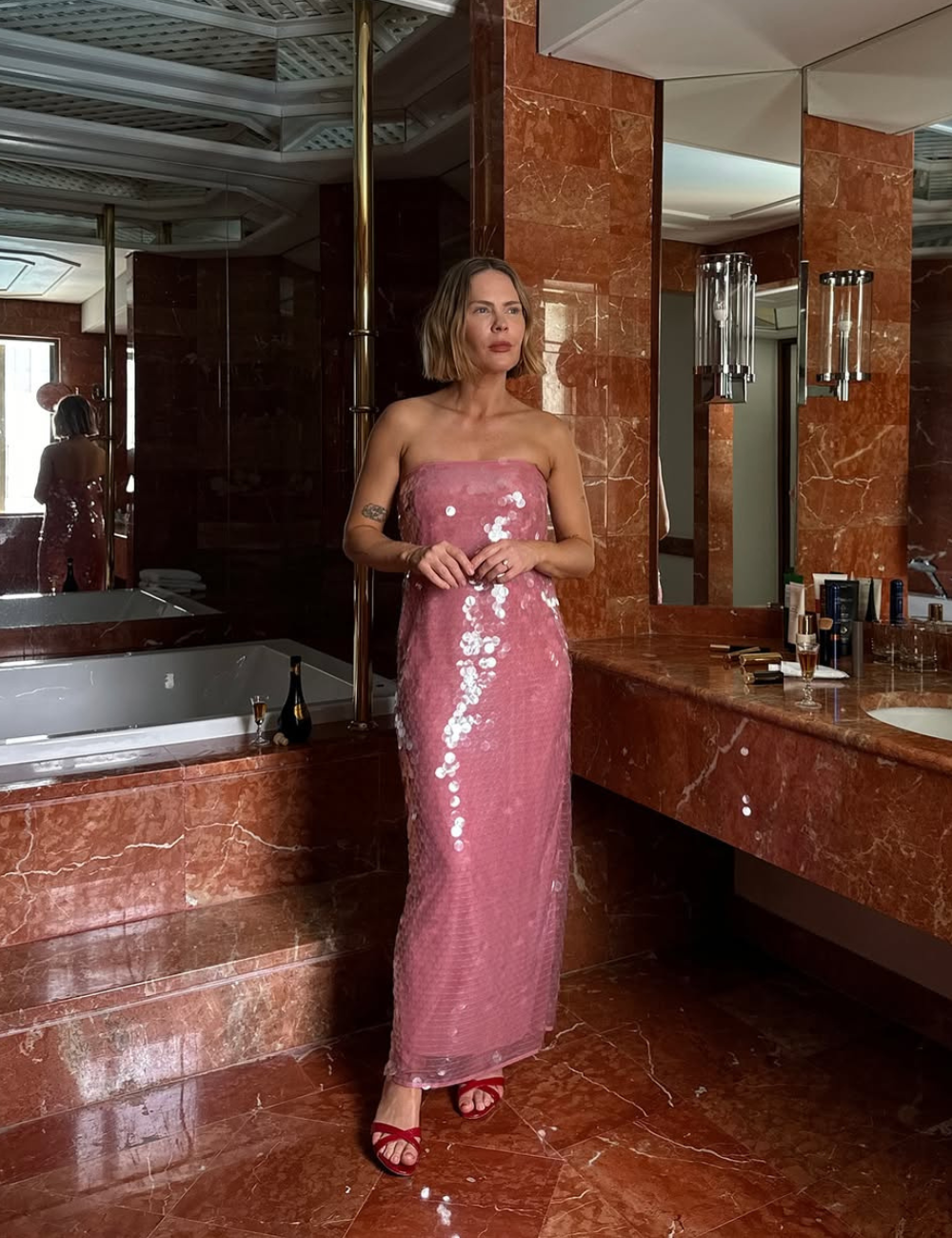 Mulher em um banheiro elegante usando vestido rosa brilhante, tendência Verão 2026.