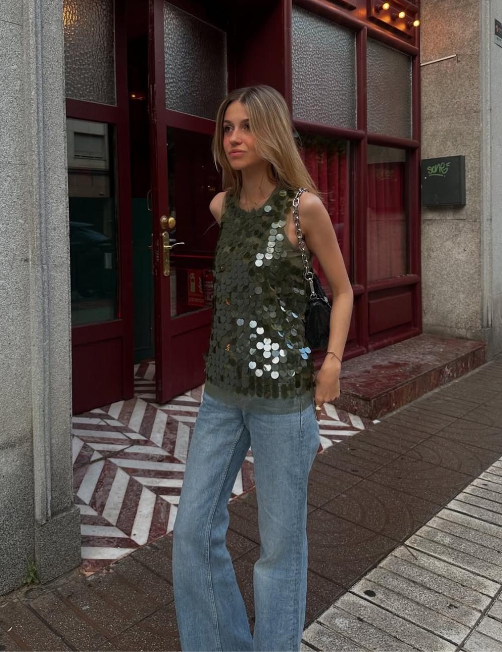 Pessoa com blusa de lantejoulas e jeans em ambiente urbano, remetendo à moda Verão 2026.