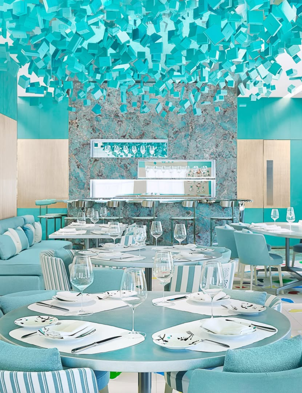 Restaurante elegante com decoração moderna em tons de azul, mesas postas, refletindo sofisticação em moda e comida.