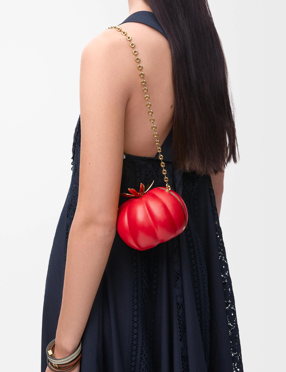 Bolsa vermelha em forma de tomate usada por pessoa com vestido azul escuro. Estilo une moda e comida.