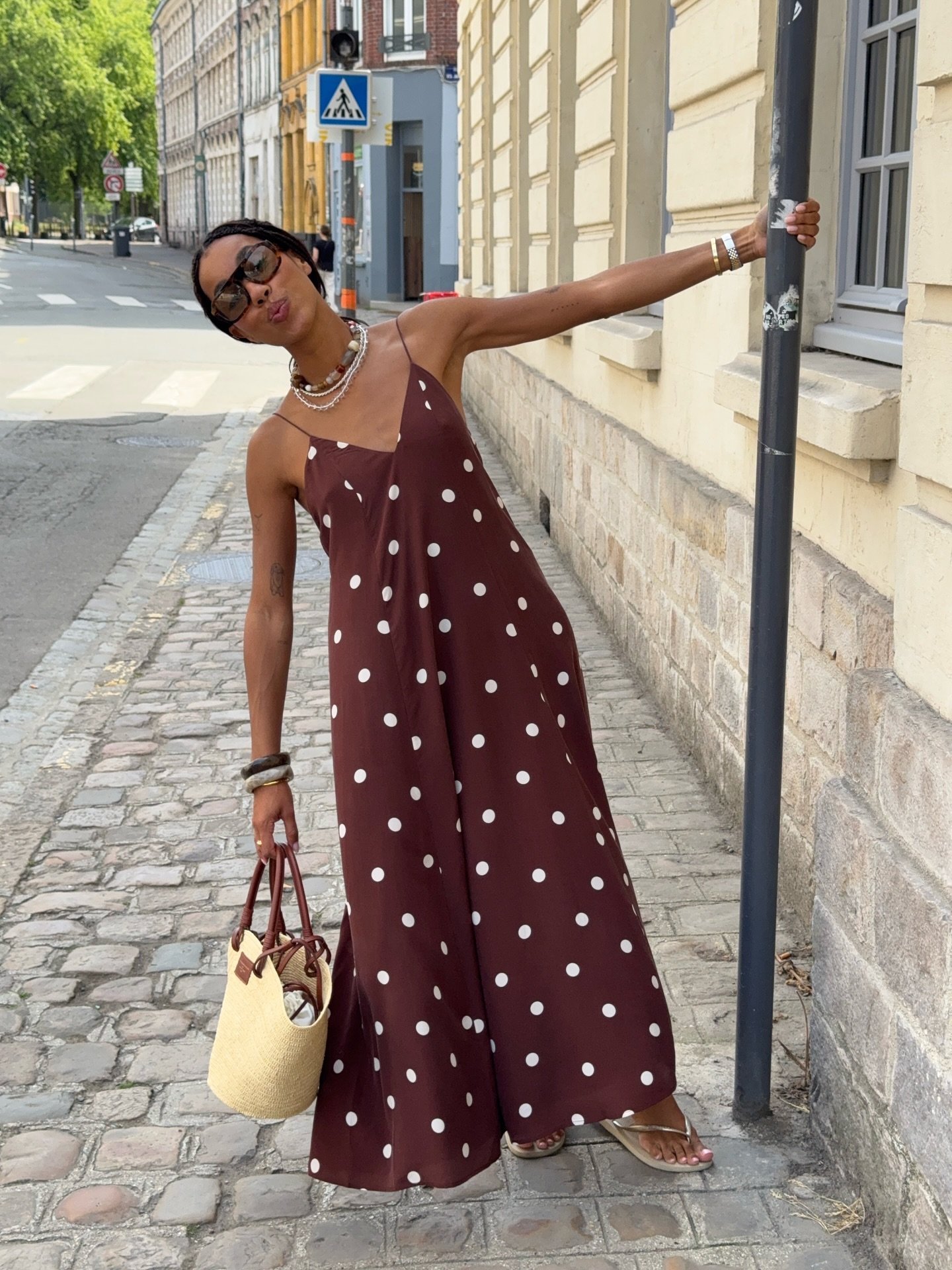 Usuária descontraída em rua de paralelepípedos, com vestido de bolinhas e modelos de sandálias.