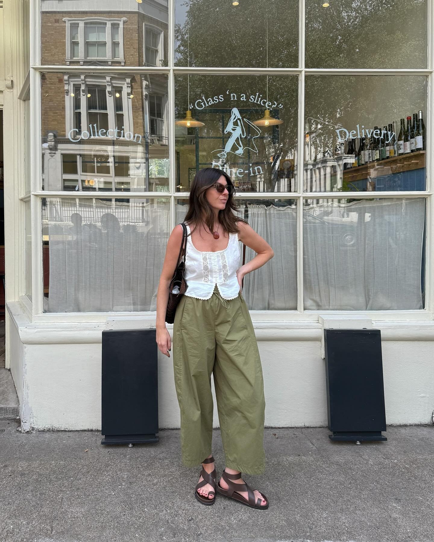 Pessoa em frente a vitrine com sandálias marrons estilosas, usando calça verde e blusa branca.