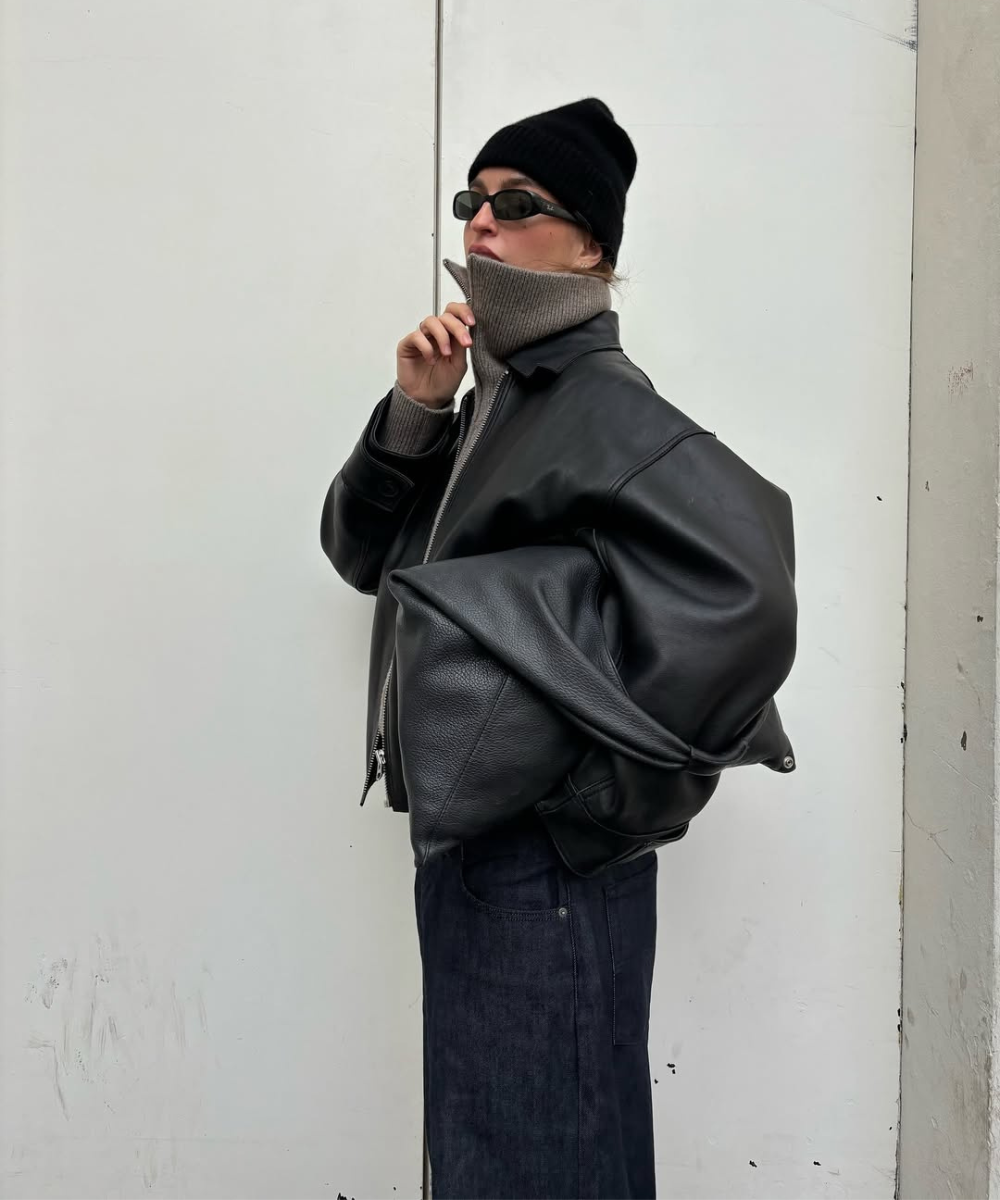 Pessoa com jaqueta de couro preta, gorro, óculos escuros e moletom com gola zíper puxada para cima.