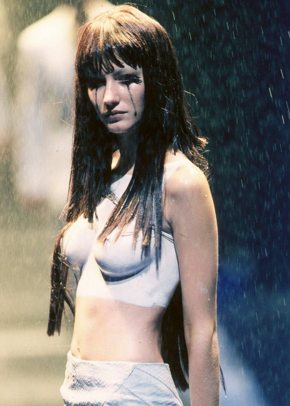 Gisele Bündchen com roupa clara sob chuva em desfile, expressando emoção dramática. Relacionado a moda e passarela.