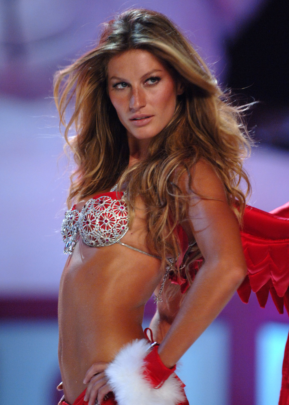 Gisele Bündchen desfilando com fantasia vermelha e branca, com detalhes brilhantes e asas.