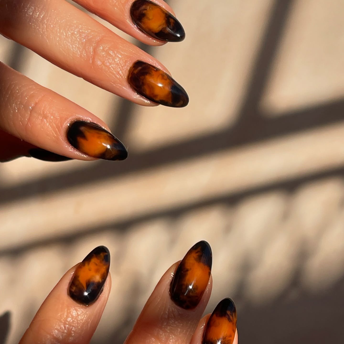 Unhas com design marmorizado em tons de âmbar e preto, destacando nail arts estilosas.
