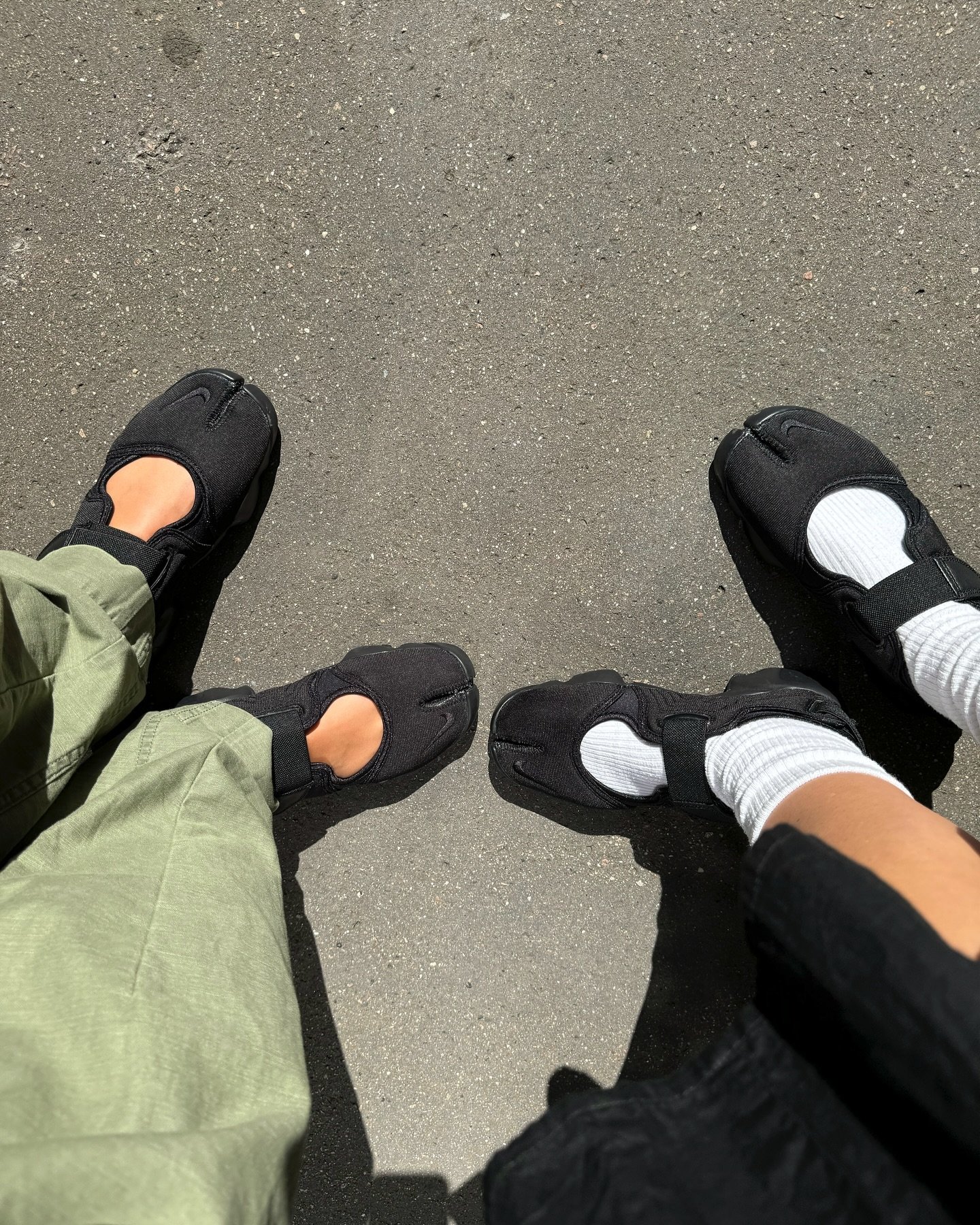 Dois pares de Nike Air Rift pretos em um piso de concreto, um com meias brancas e outro sem.