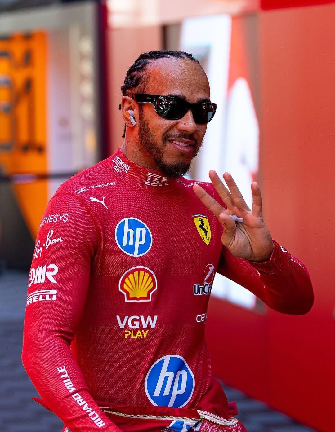 Pessoa usando óculos de sol do momento, com roupa de corrida vermelha cheia de logotipos, fazendo gesto com a mão.