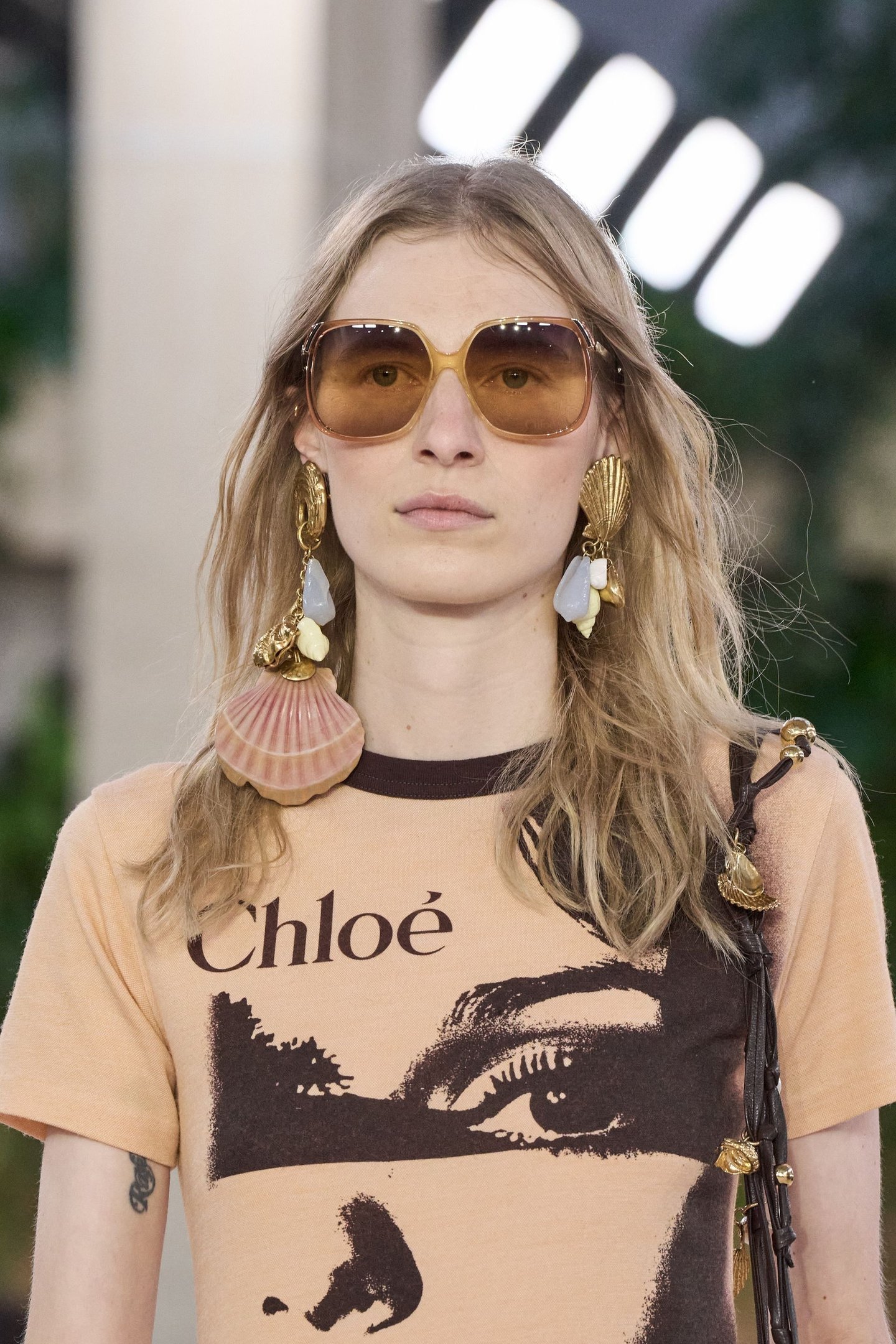 Óculos de sol grandes e brincos largos usados em conjunto com camiseta Chloé, estilo acessório boho.