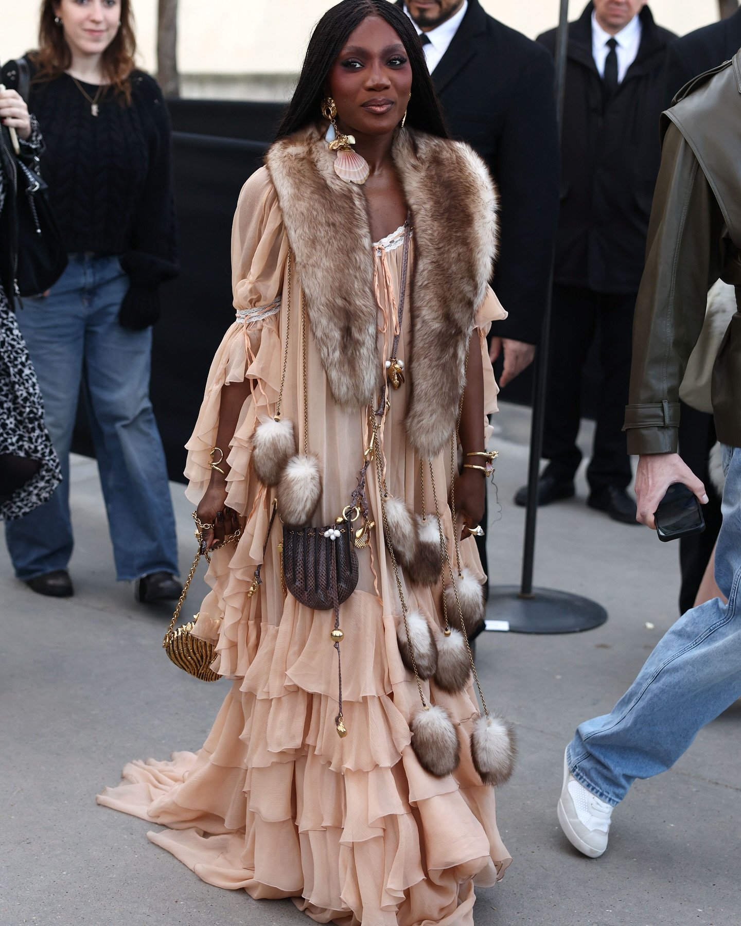 Vestido de babados com acessórios boho, incluindo bolsa de penas e brincos grandes, em um evento de moda.