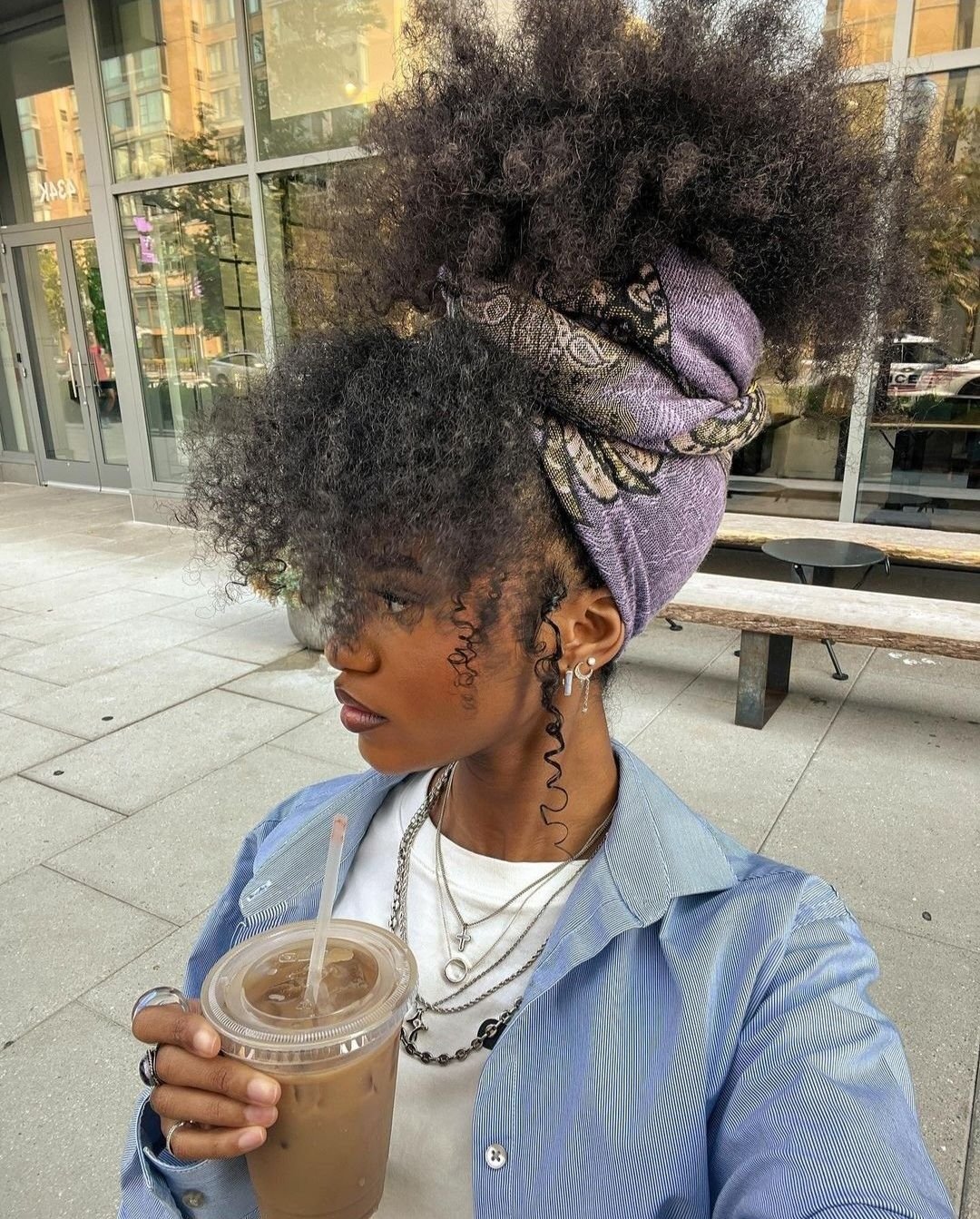 Pessoa com cabelo volumoso preso em penteado solto e sem tração, usando tiara colorida e segurando bebida.