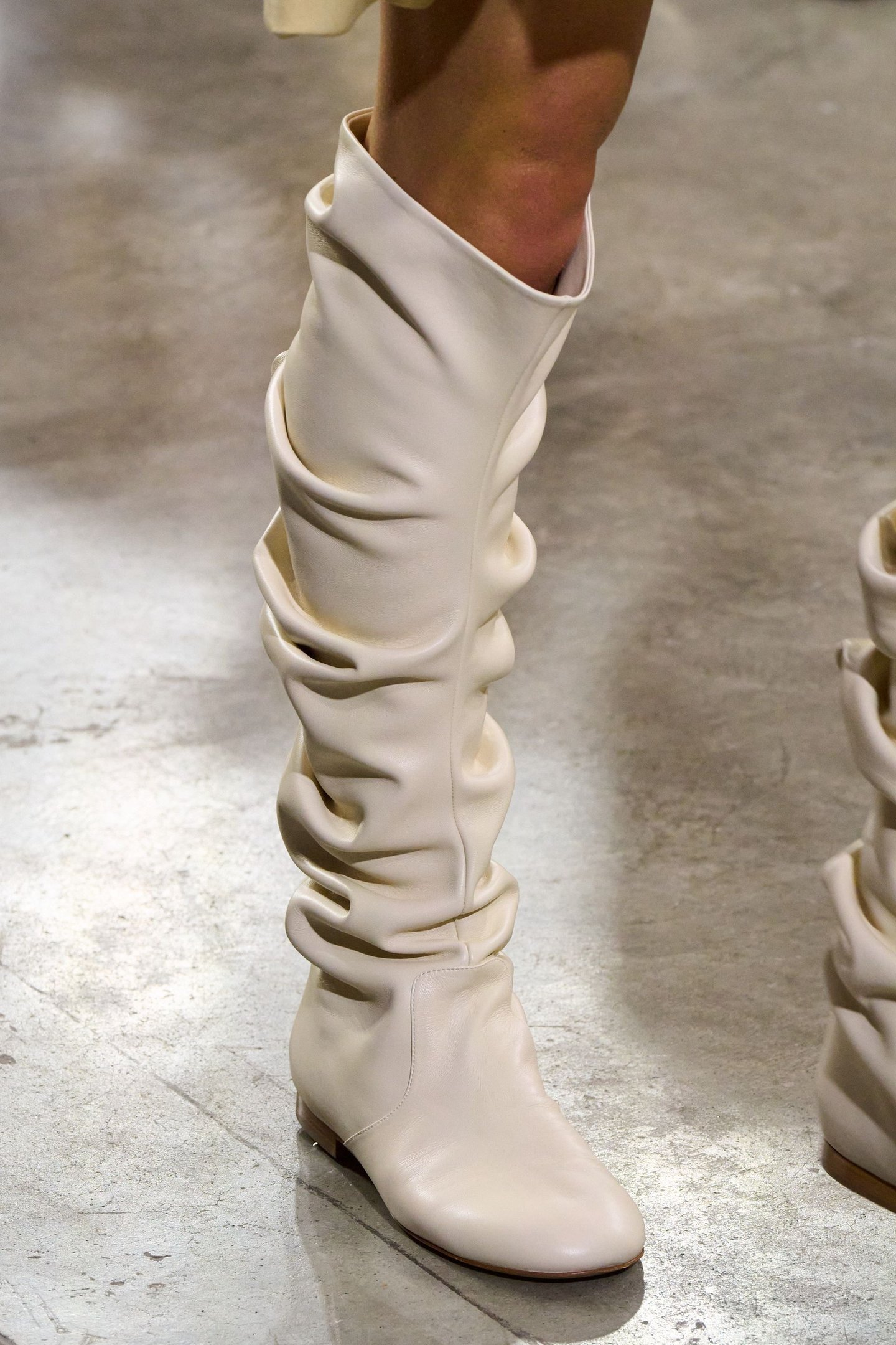 Bota branca com cano franzido e salto baixo em um piso de cimento.