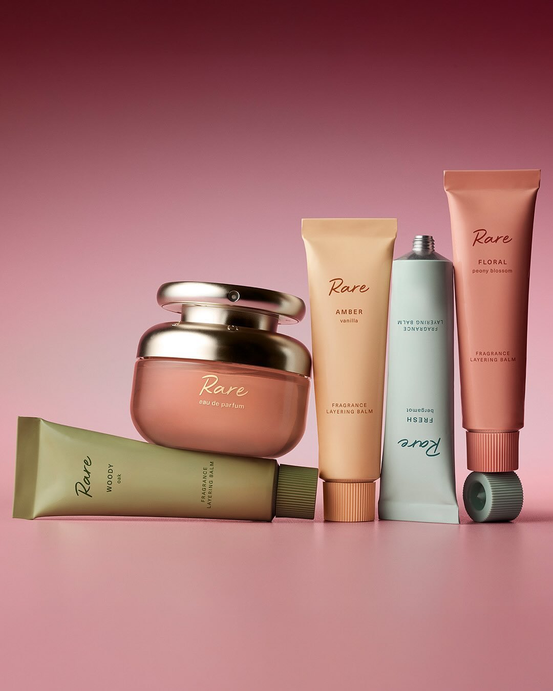 Conjunto de frascos e tubos de perfumes Rare, de cores e aromas variados, sobre fundo rosa.