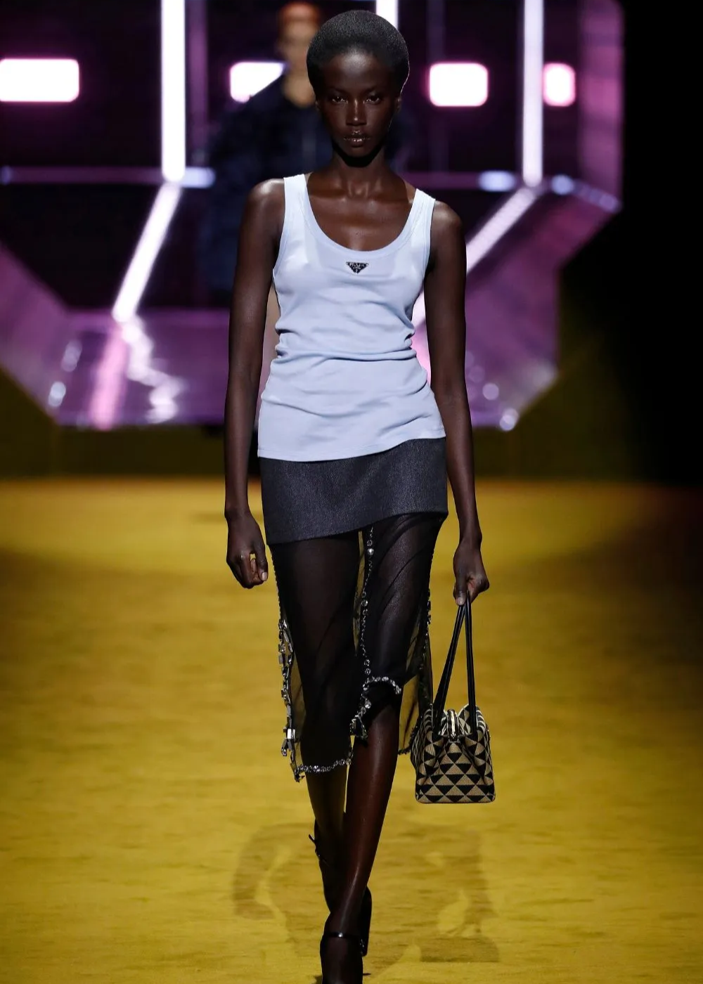 Modelo de regata branca e saia preta transparente em passarela iluminada.