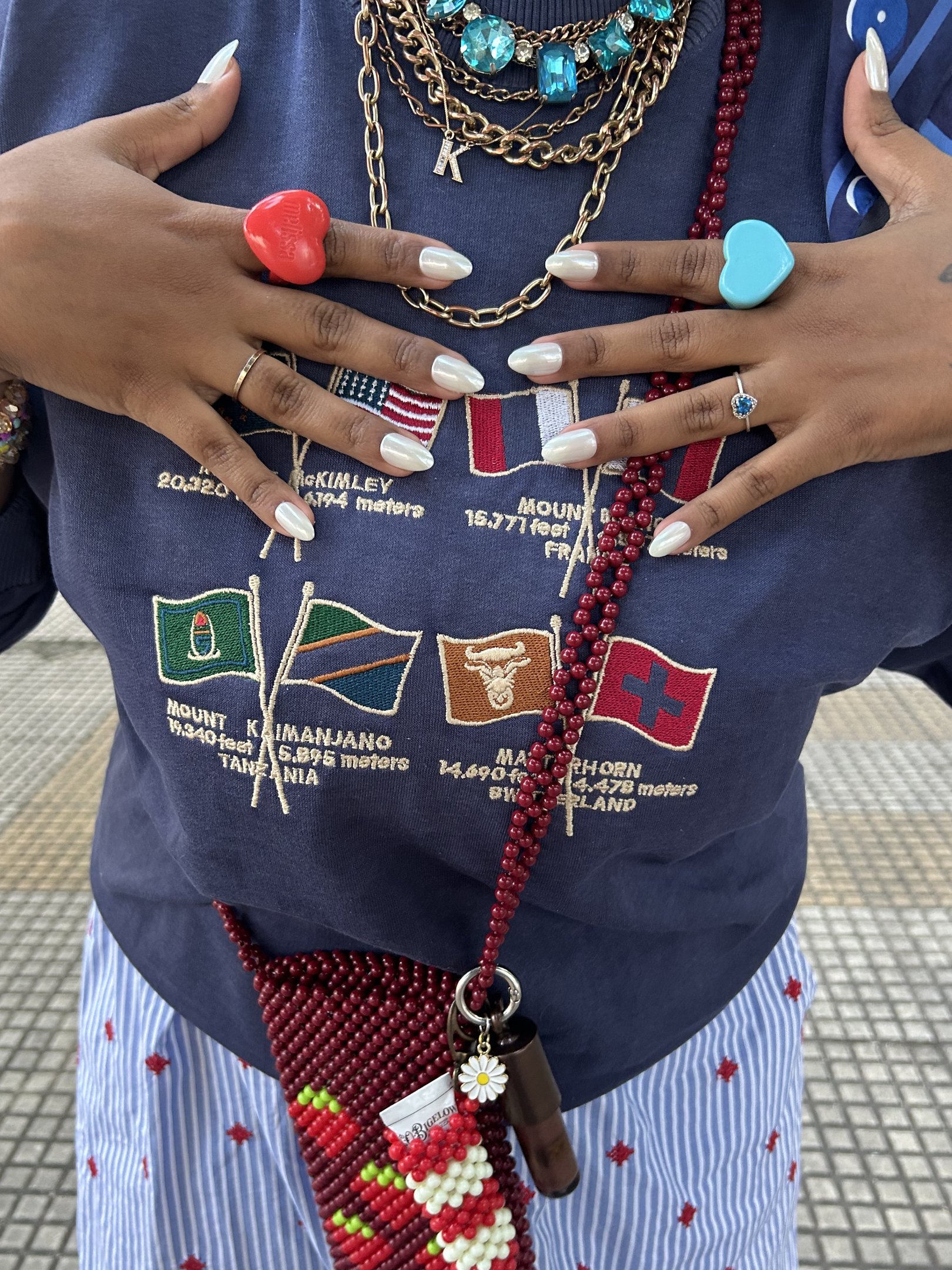 Pessoas exibem unha autocolante branca e anéis coloridos sobre roupas com estampa de bandeiras.