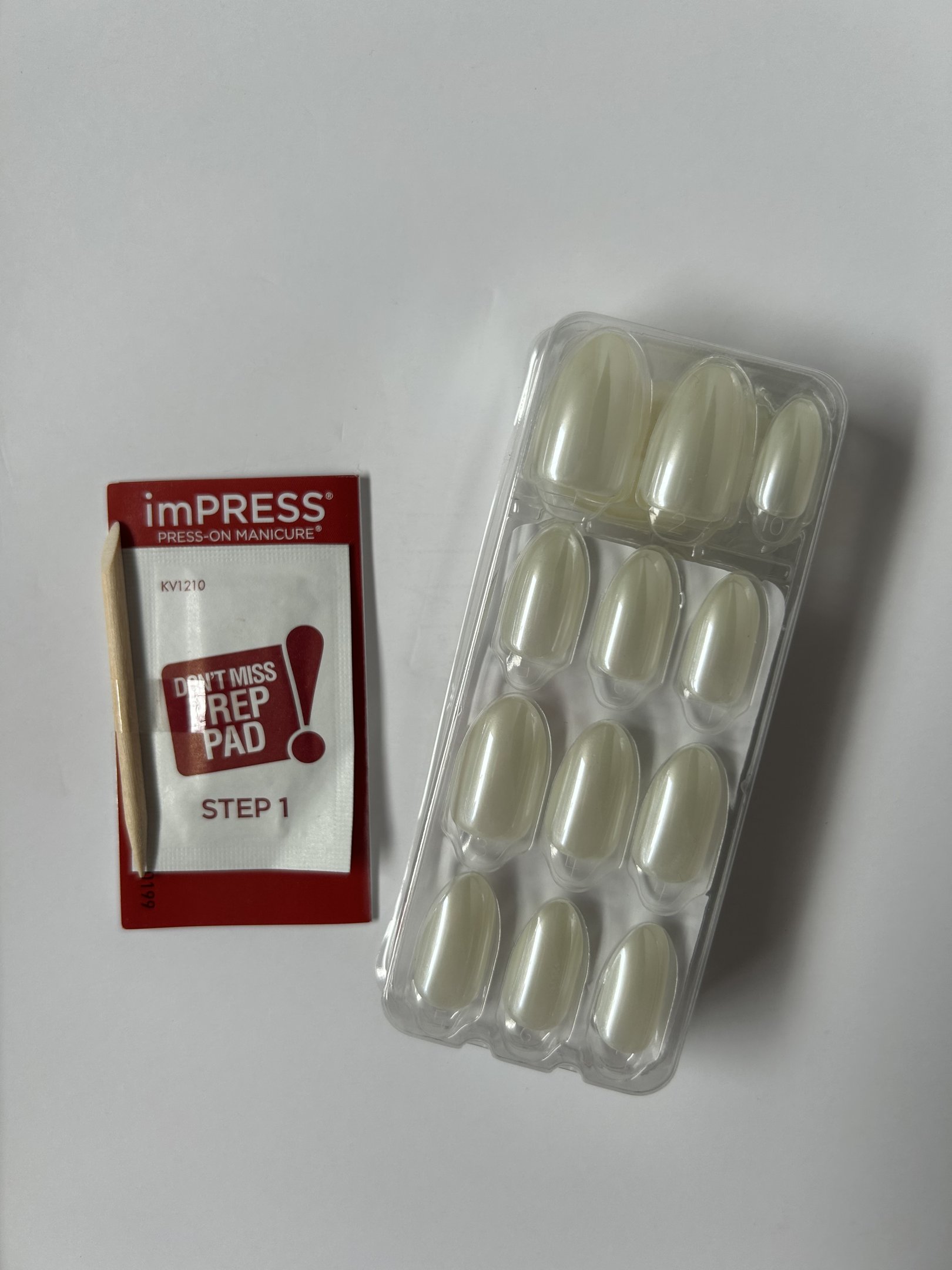 Conjunto de unhas autocolantes em embalagem transparente ao lado de um palito e um sachê de preparação.