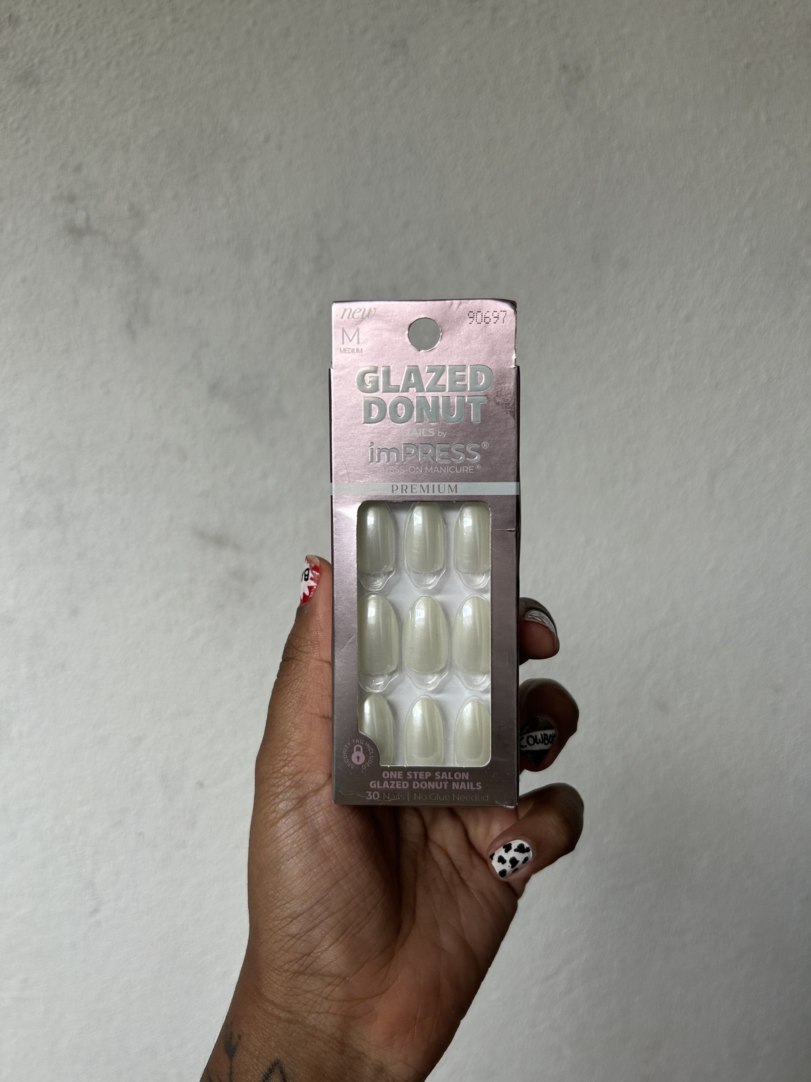 Unha autocolante branca em embalagem, segurada por mão com unhas decoradas.